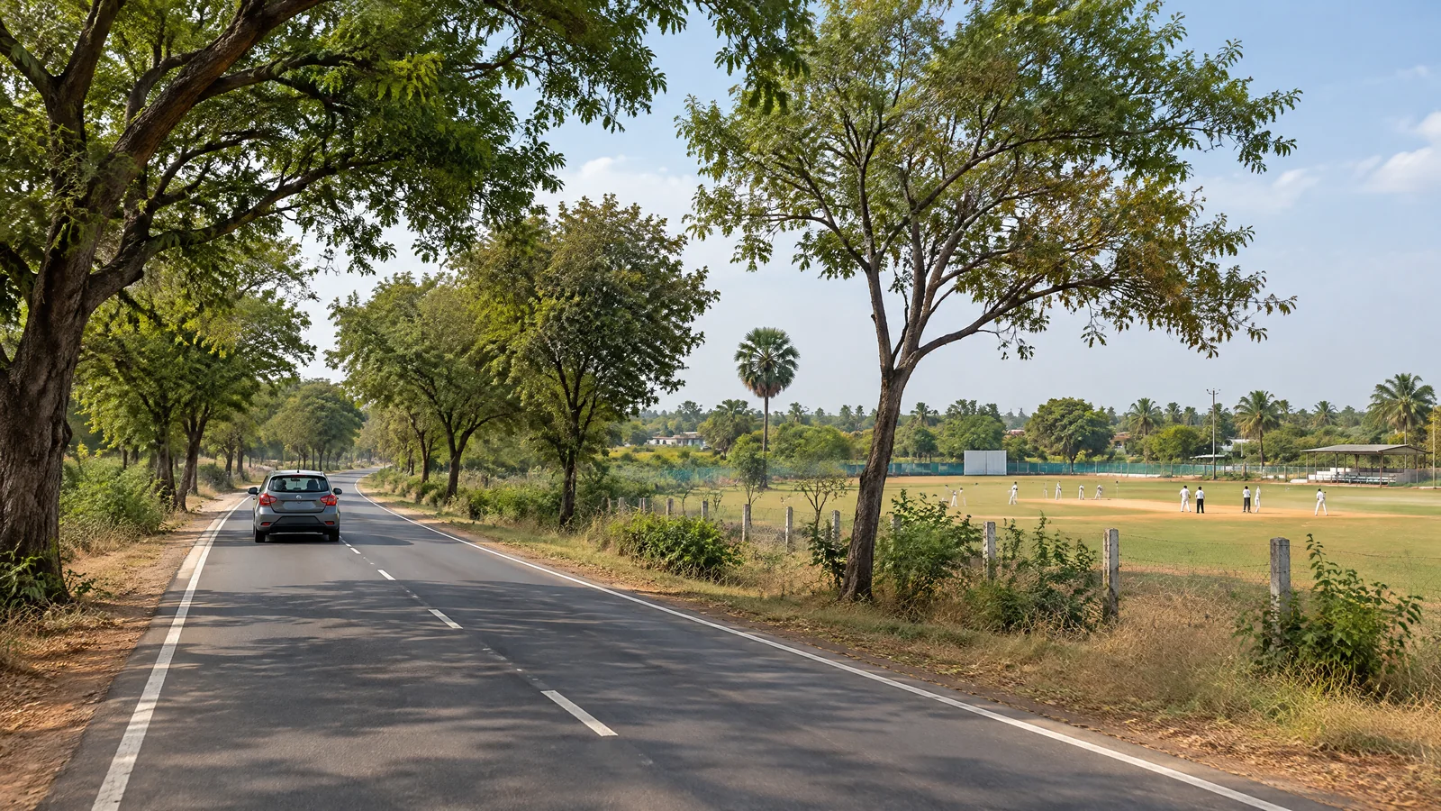 Car on an inland road beside a modest cricket field